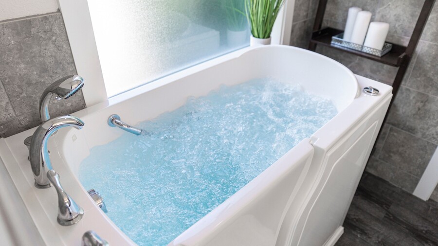 Walk-in bathtub filled with bubbling water in a modern bathroom with chrome fixtures and gray tile walls